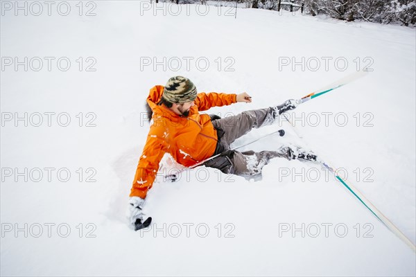 Caucasian man falling on cross-country skis in snow