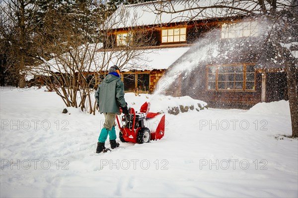 Caucasian man using snow blower in snowy driveway