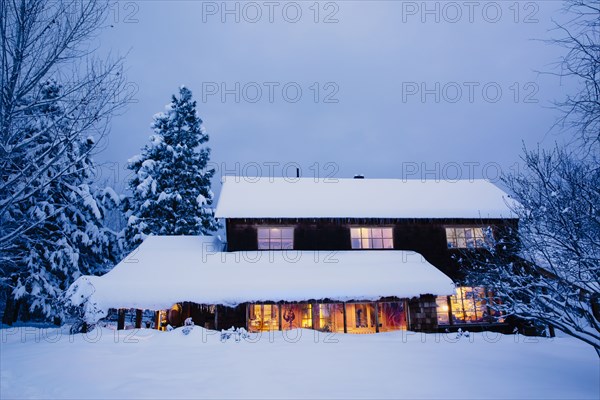 Illuminated house in snowy field at dusk