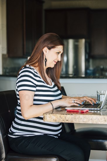 Pregnant Hispanic woman using laptop in kitchen