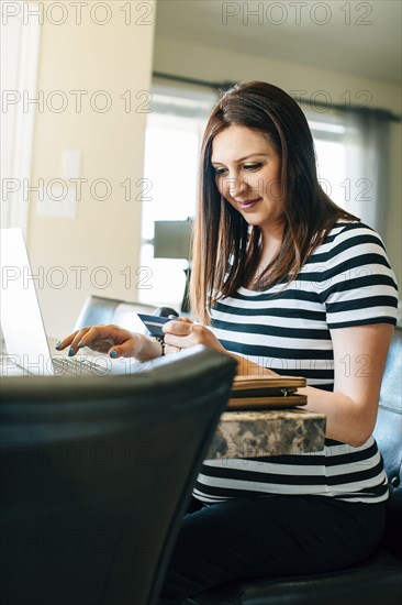 Pregnant Hispanic woman shopping with laptop in kitchen