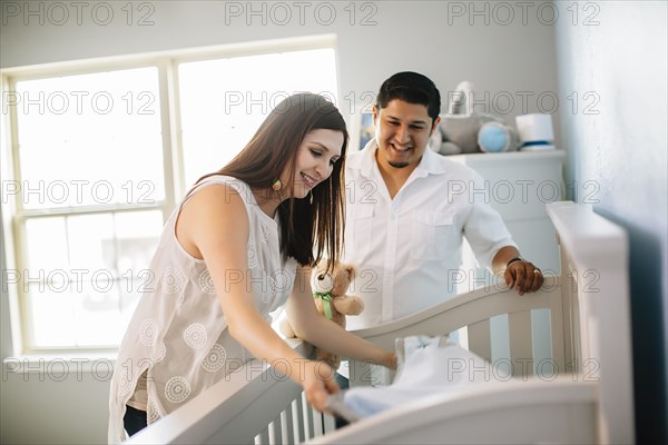 Hispanic couple preparing crib bed in nursery