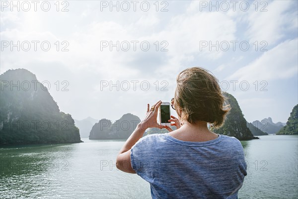 Caucasian woman photographing rock formations in Ha Long Bay