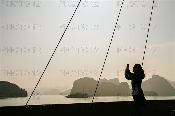 Caucasian woman photographing rock formations in Ha Long Bay