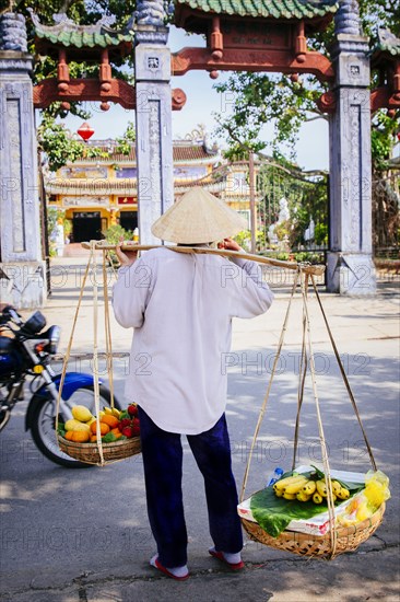 Vendor carrying fruit baskets on city sidewalk