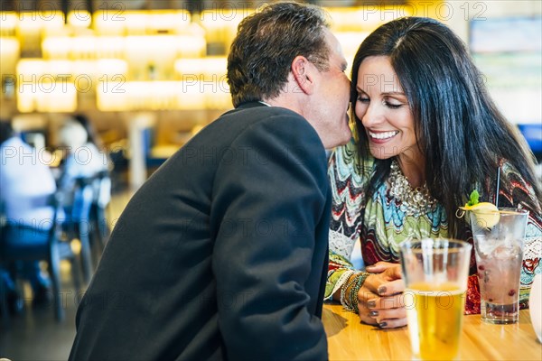 Caucasian man whispering to ear of woman in restaurant
