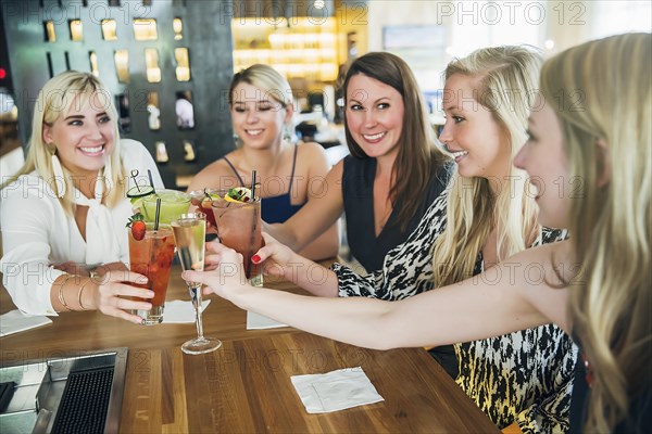 Caucasian women toasting at bar with cocktails