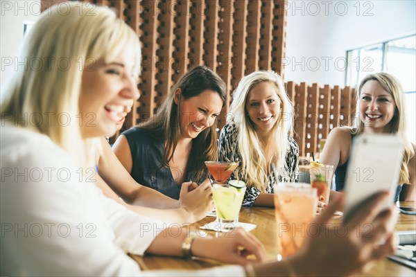 Caucasian women at bar with cocktails taking selfie