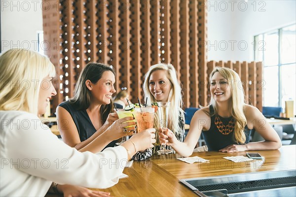 Caucasian women toasting at bar with cocktails