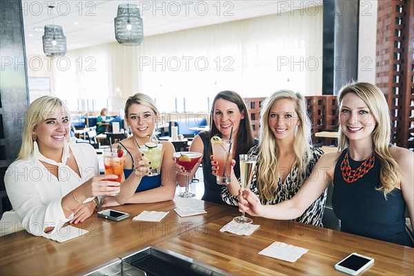 Caucasian women toasting at bar with cocktails