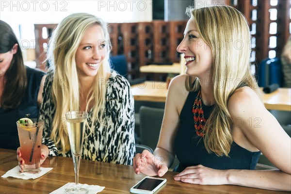 Smiling Caucasian women at bar with cocktails