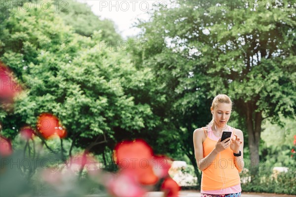 Caucasian woman using cell phone and earbuds outdoors