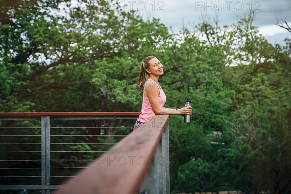 Caucasian woman leaning on banister holding water bottle