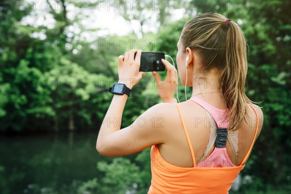 Caucasian woman using earbuds photographing with cell phone