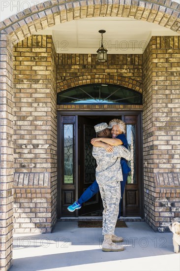 Black soldier hugging wife in doorway