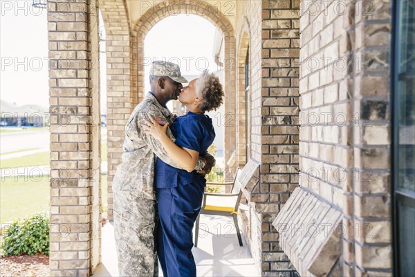 Black soldier kissing wife on front stoop