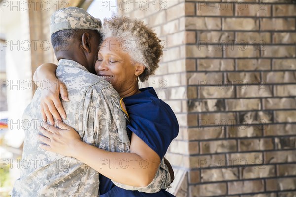 Black soldier hugging wife on front stoop