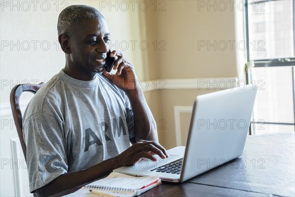 Black man using laptop and cell phone at table