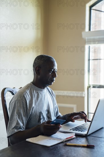 Black man using credit card with laptop at table