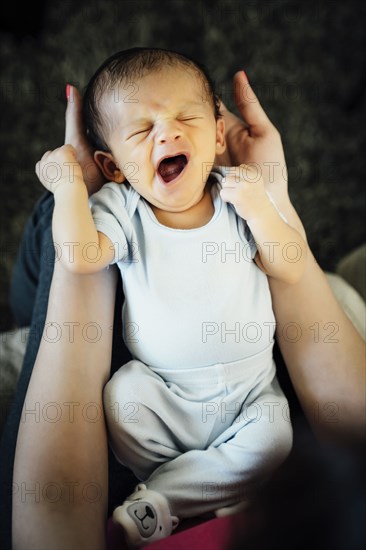 Hispanic woman holding yawning baby boy in lap