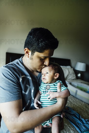 Hispanic man kissing forehead of baby boy