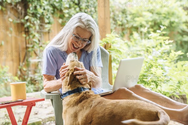 Caucasian woman using laptop petting dog on backyard patio