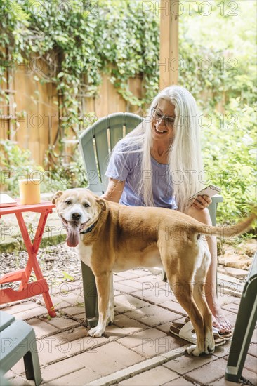 Caucasian woman holding cell phone petting dog on backyard patio