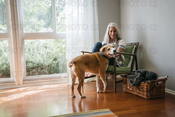 Caucasian woman sitting in armchair petting dog