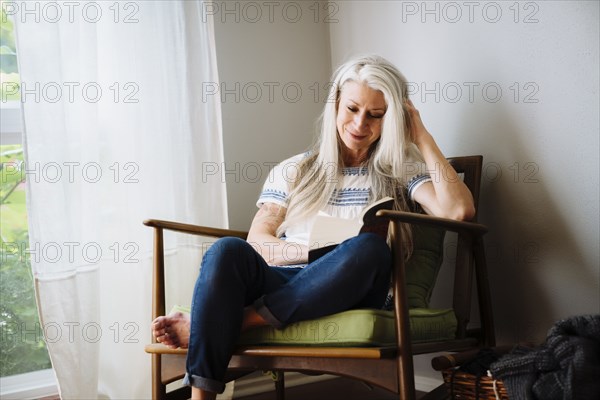 Caucasian woman sitting in armchair reading book