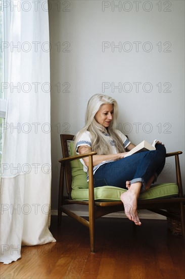 Caucasian woman sitting in armchair reading book