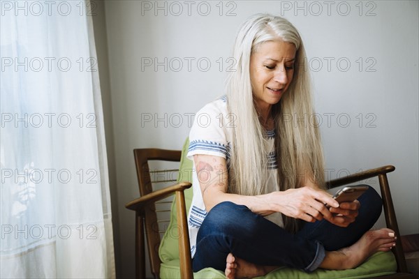 Caucasian woman sitting in armchair texting with cell phone