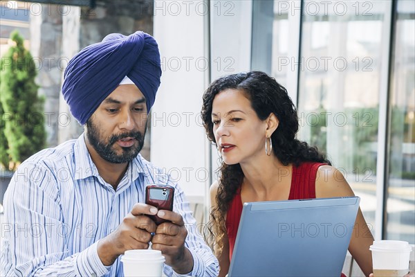 Man and woman using cell phone and laptop at cafe