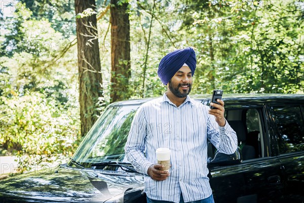 Man wearing turban posing for cell phone selfie at car