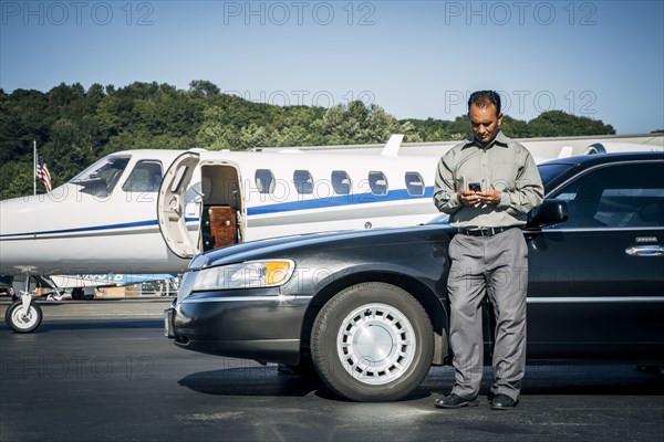 Indian man texting on cell phone at car near airplane