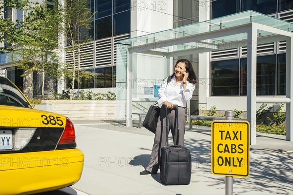 Businesswoman talking on cell phone near taxi