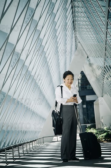 Businesswoman standing in lobby with suitcase texting on cell phone