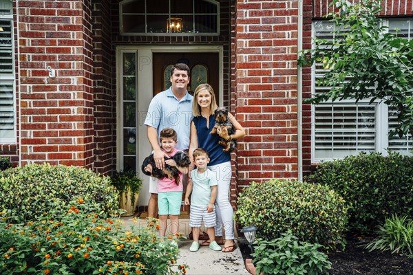 Proud Caucasian family posing at front stoop of house with dogs