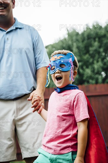 Caucasian father and superhero son holding hands