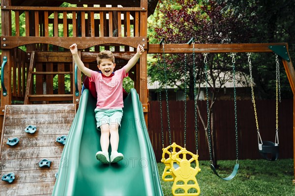 Caucasian boy sliding on backyard playground slide