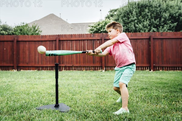 Caucasian boy hitting baseball off tee in backyard
