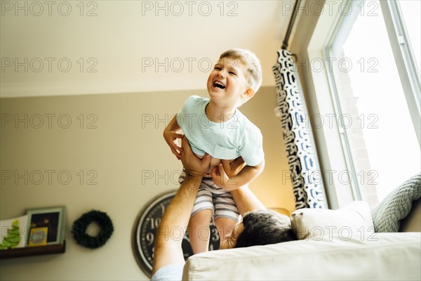 Caucasian father laying on sofa lifting son