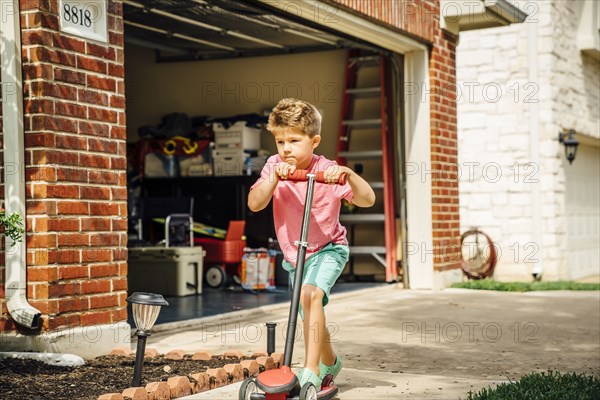 Caucasian boy riding push scooter in driveway