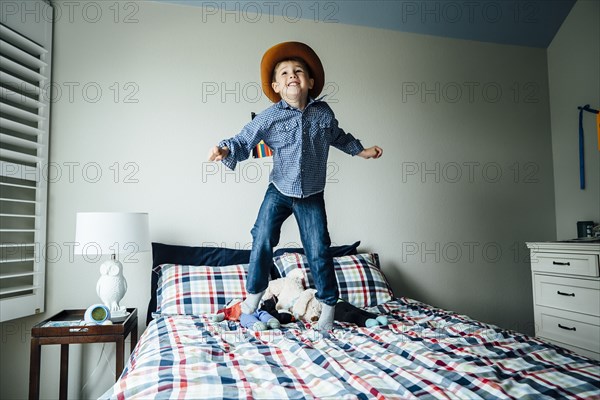 Caucasian boy wearing cowboy costume jumping on bed