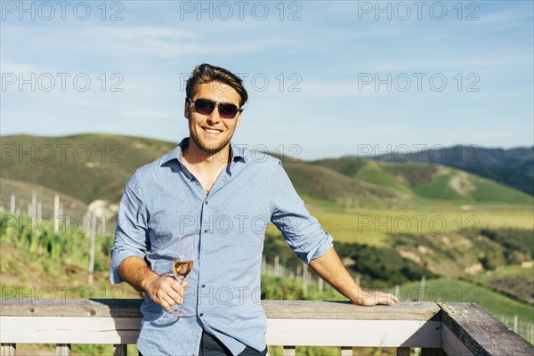 Caucasian man leaning on balcony drinking wine