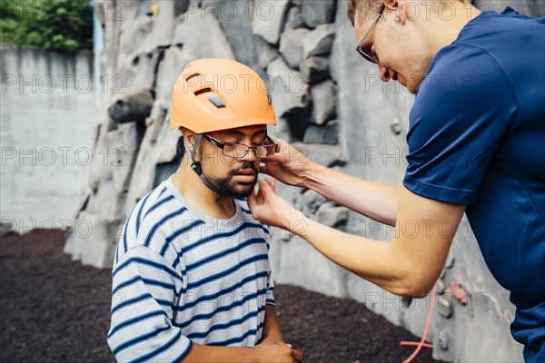 Man helping rock climber fasten helmet