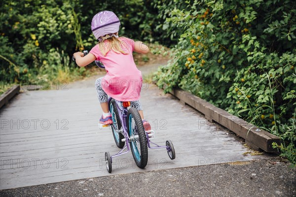 Mixed Race girl riding bicycle with training wheels