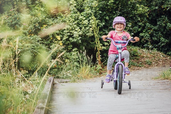 Mixed Race girl riding bicycle with training wheels