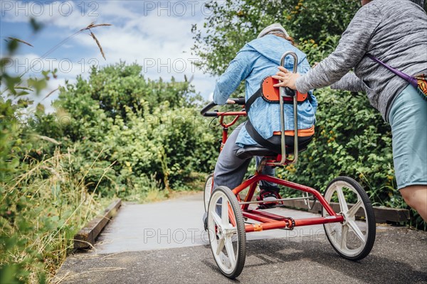 Caucasian woman pushing daughter riding tricycle