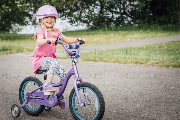 Mixed Race girl riding bicycle with training wheels