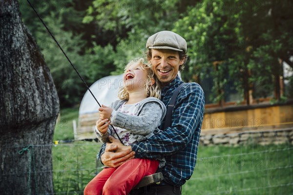 Caucasian man hugging daughter on rope swing